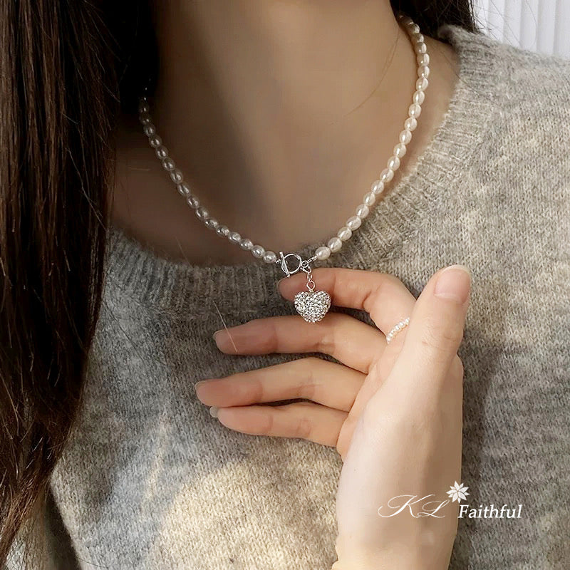 Pearl necklace with a heart-shaped pendant worn by a person in a gray sweater.
